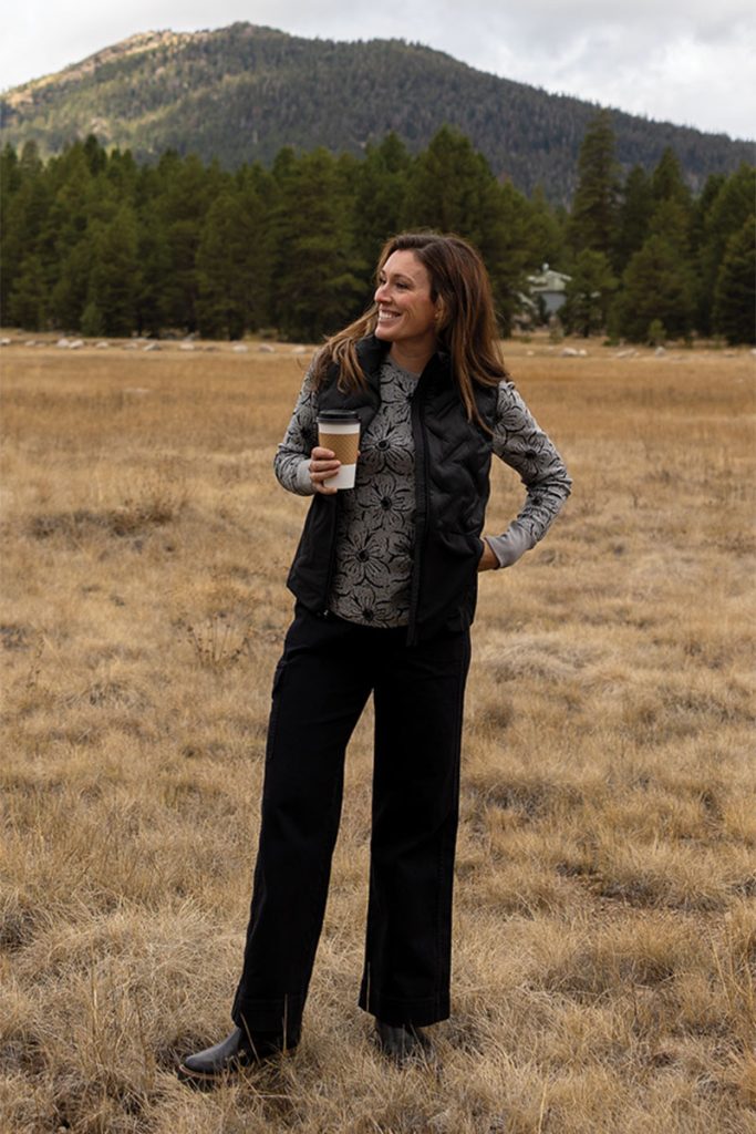 Woman standing in field during fall with coffee in hand.