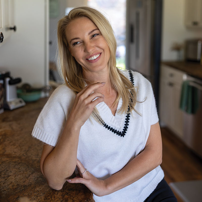 Woman sitting at kitchen counter top in white vest.