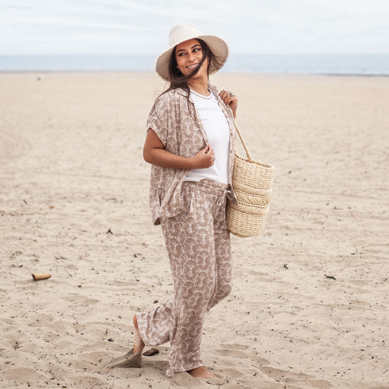 Woman standing on sandy beach with bag over shoulder.