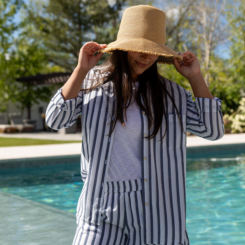 Woman standing near pool outside with sun hat on.