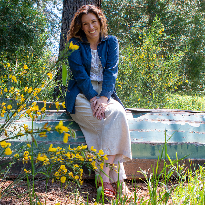 Woman sitting on old rustic boat outside in front of flowers.