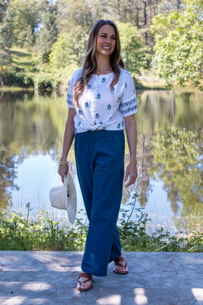 Woman standing next to pond outdoors with sun hat in hand.