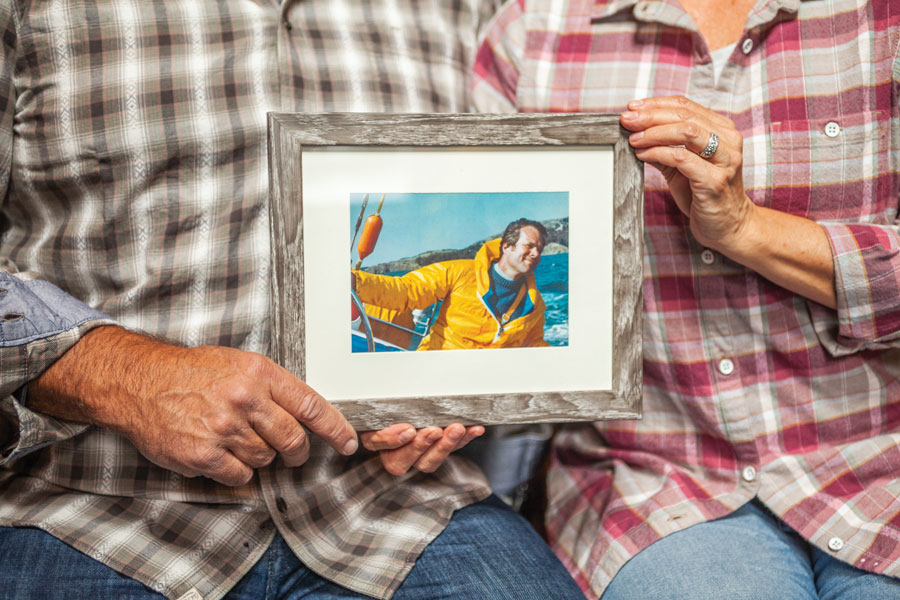 Kirsch siblings holding framed photo of John Kirsch sr. on sail boat.